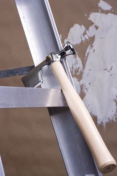 Drywall hammer on a step ladder next to a brown drywall.