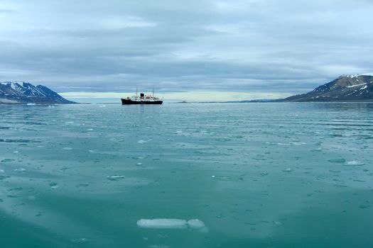 Cruise ship sailing through melting ice and icebergs in a fjord in Spitsbergen, Svalbard.