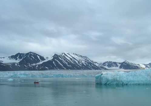 Small rubber boat sailing through melting ice and icebergs in a fjord in Spitsbergen, Svalbard.