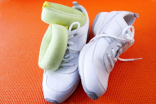 Close up of white sneakers and light green wrist bands on an orange yoga mat reflect readiness for exercise and fitness