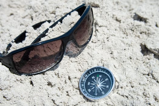 Sunglasses and compass in the sand