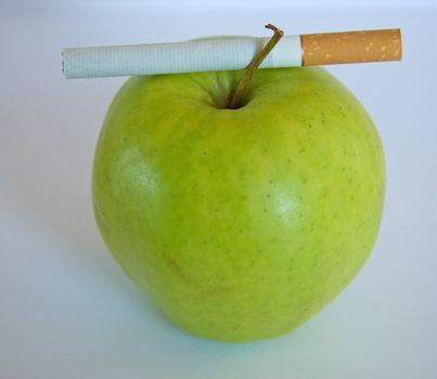 Cigarette lying on a top of a green apple.