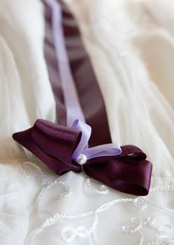 Close on a purple ribbon on a beautiful white christening gown with laces.