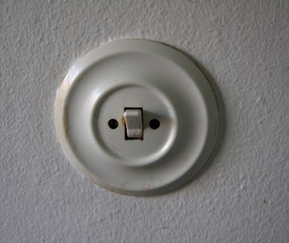 Old round white switch on a white wall.