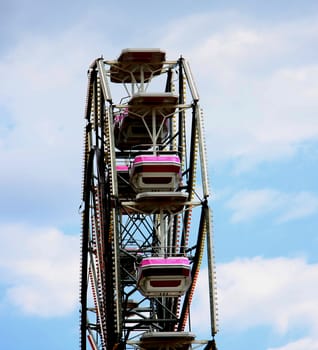 Ferris wheel with pink swings with cloudy skyin the background.