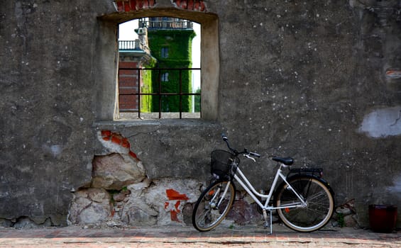 Bike parked by a window in an old wall. A castle is seen in the window.