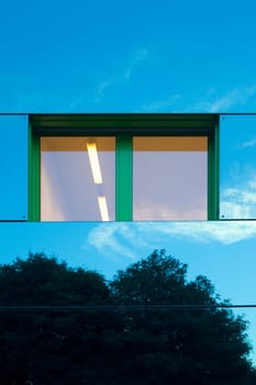 Mirrored image of environment of office building on highly reflective exterior wall with window.