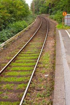 Deserted single track railway stop in green rural setting.