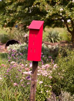 Red painted bird house in flowery garden with small slits for the bird to enter