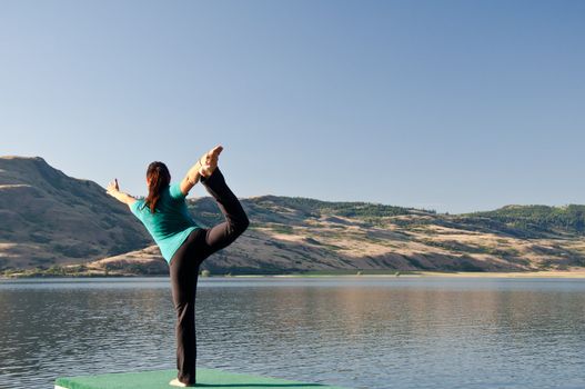 Young fit girl practicing Yoga in the Dancers pose next to a calm lake