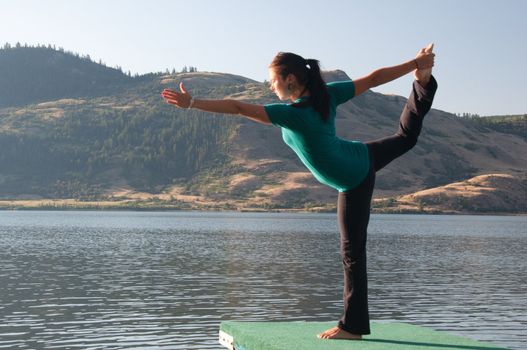 Young fit girl practicing Yoga in the Dancers pose next to a calm lake