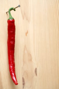 Red hot chili pepper hanging with nail on wooden background