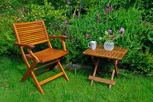 A hardwood garden chair and table, cup of coffe and a vase with flowers.