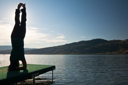 Young fit girl meditating in a headstand pose by a calm lake