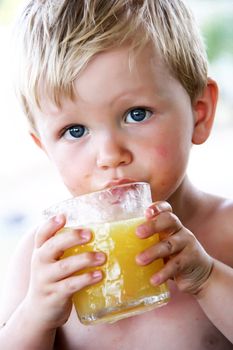 little boy with blue eyes is drinking his orange juice