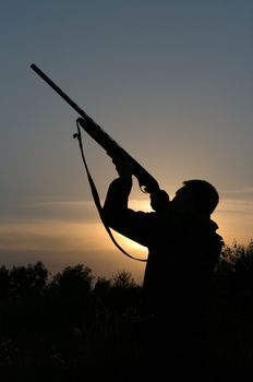 Silhouette of the hunter with a gun against the evening sky.