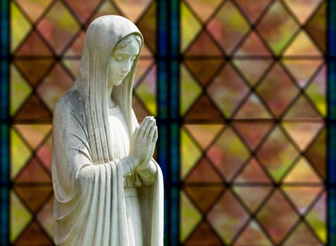 Statue of Mary praying in profile with isolation path and out of focus window as background