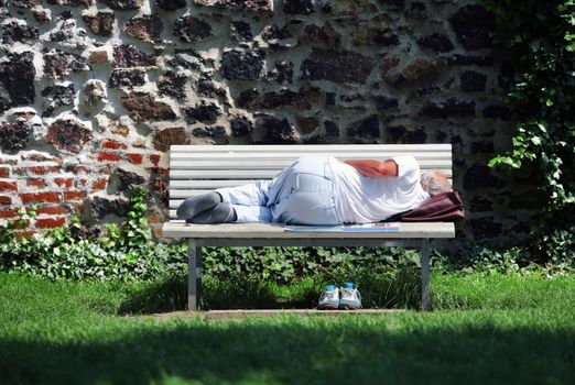 Old man sleeping on the bench in park with bag under his head