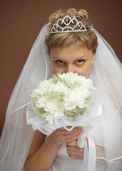 Portrait of the bride with a bunch of flowers at the face on a brown background