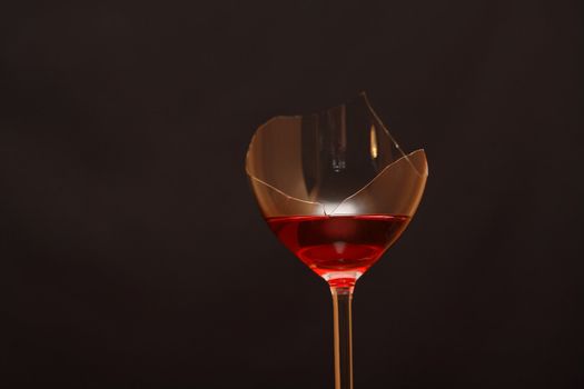 Broken wineglass with red wine on dark background