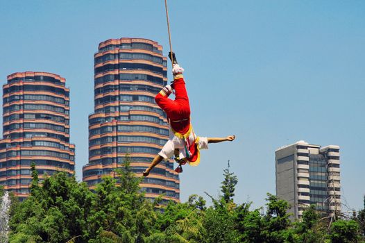 Builder hanging by one leg up side down on the rope with Mexico city on background