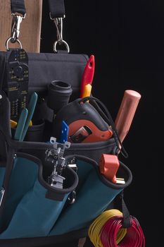 Electrician's bag with tools on a black background.