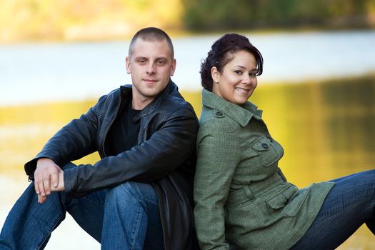 A happy interracial couple sitting outdoors by a lake or pond.