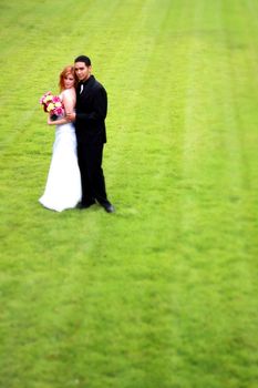A bride and Groom stading on a green lawn