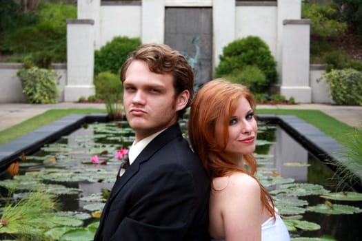 A bride and a groom sit by a lily pond