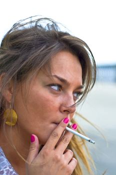 Young beautiful girl smokes. Purple manicure. Summer portrait on the beach. Blured focus.