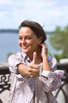 Young beautiful girl holds a raised upper finger. Focus on the hand, even background blur. Summer portrait.