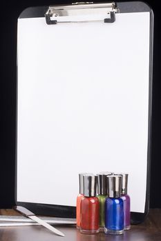 Nail polish bottles standing in front of a clip pad with white paper. Add your text to the paper.