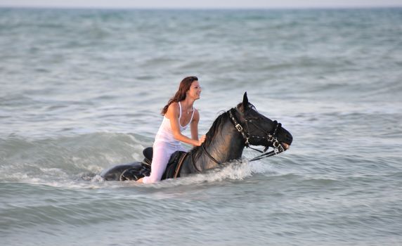 young woman swimming winth her black stallion in the sea