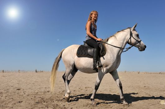 young teen and her white horse on the beach, sun with halo in the sky