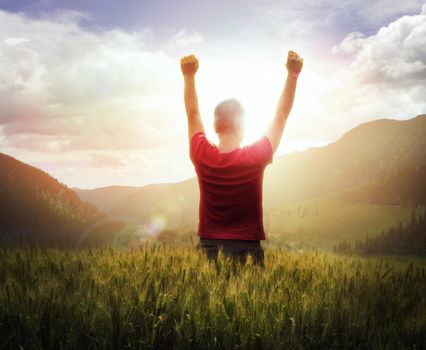 Young man with arms raised looking at sunset with mountains ahead