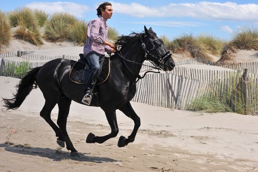 galloping black stallion and his rider on the beach