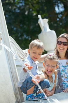 Beautiful Mother with her kids playing with water in fountain. Vertical view