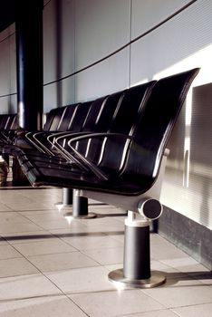 A line of empty chairs in the airport of amsterdam, black chairs lighted by the evening's sun. 