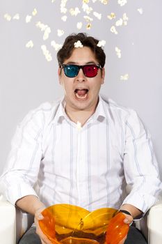 A young man watching a movie in 3D, with stylish 3D glasses and eating popcorn. He got so scared he threw his popcorn into the air.