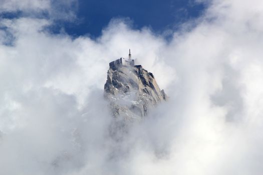 View of Aiguille Du Midi surrounded by lots of clouds and deep blue sky from Chamonix, France