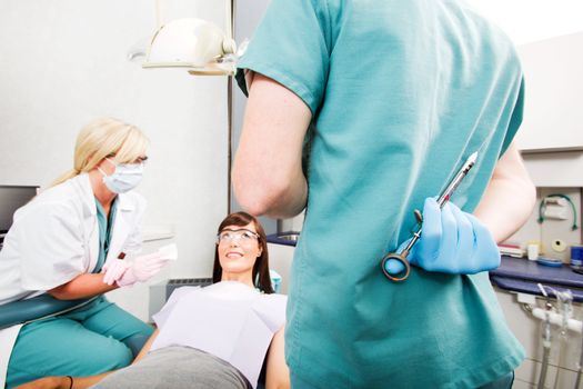 A dentist with a big needle behind his back and a worried patient