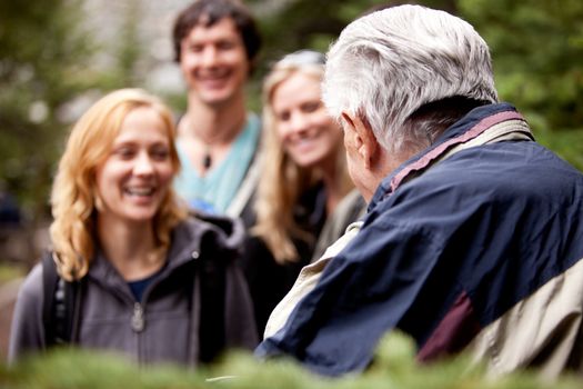 An elderly man talking to a group of young people in the forest.