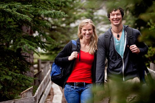 A man and woman on a hike in the forest, smiling at the camera