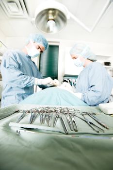 A row of sterile surgery instruments with live surgery being performed in the background