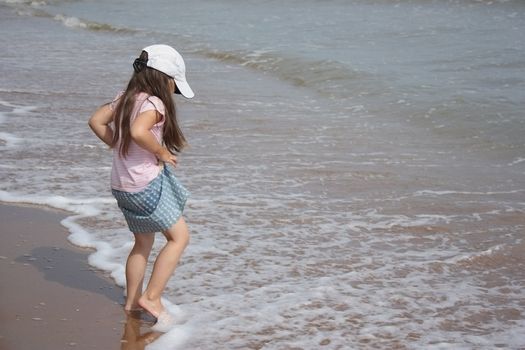 Preschool girl on the beach soaks his feet