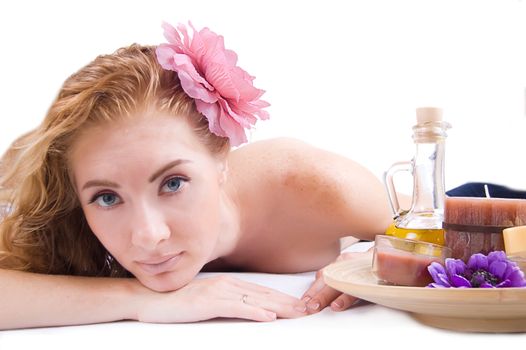 Redheaded woman lying with spa products over white