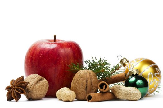 red apple, star anise, some nuts, golden and green christmas balls and a branch on white background