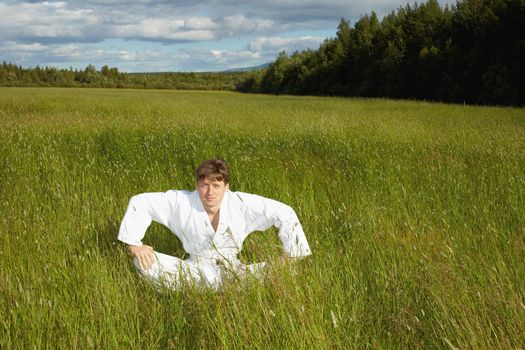 The young man sits in a grass in the field