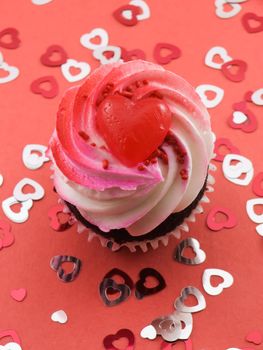 Valentines cupcake on red with several confetti hearts