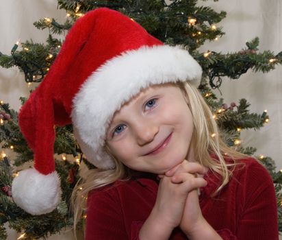 Young girl wearing a santa hat with christmas tree behind her